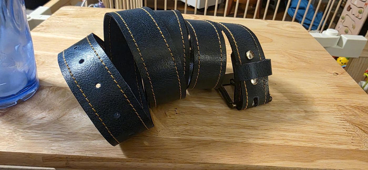 Hand-dyed leather belt with double stitching, coiled on a workbench
